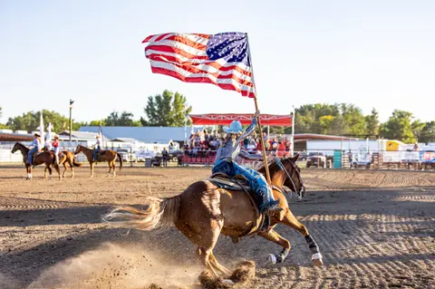 A person rides a horse carrying an American flag in an arena.