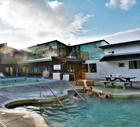 People relax in hot springs pools outside a building with murals.