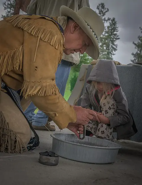A man in historical attire and a young child look into a metal basin.