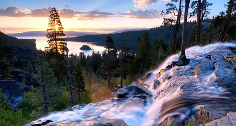 A scenic landscape view of a waterfall with a lake and sunset in the background.