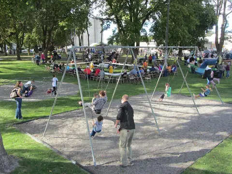 An outdoor park with people on swings and gathered at picnic tables.