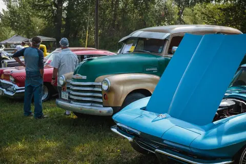 People looking at classic cars parked in a grassy area.