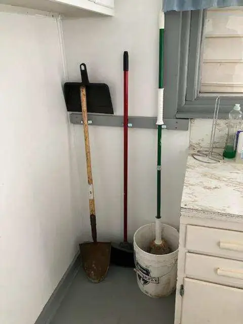 Cleaning tools leaning against an indoor wall next to a counter.