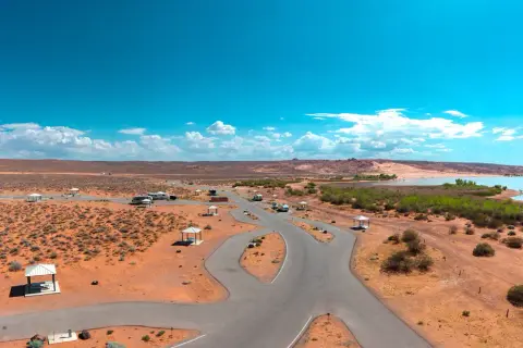An aerial view of a desert campground with paved roads and picnic shelters near a body of water.