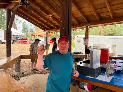 A man holds up a small cup at an outdoor wooden pavilion.