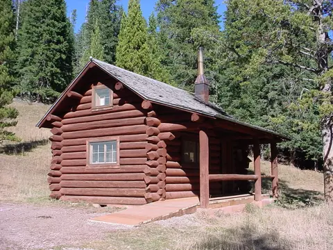 A wooden log cabin nestled in a forest of tall pine trees.