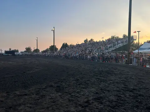 A large crowd fills the stands at an outdoor arena during sunset.