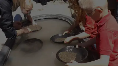 Children pan for gold in a round tub filled with water and dirt.