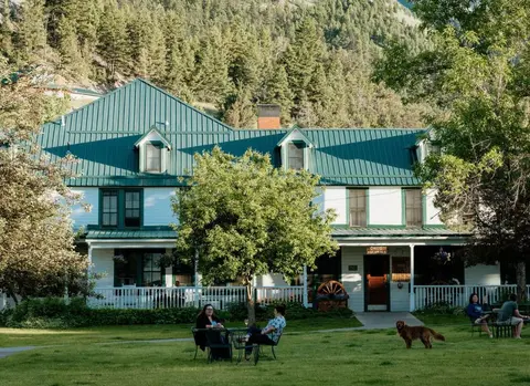 People relaxing on a lawn in front of a white building with a green roof.