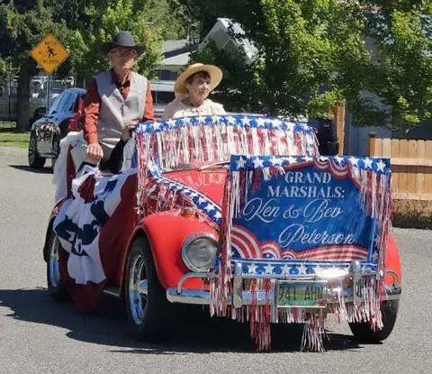 A decorated red convertible car carrying two grand marshals in a parade.