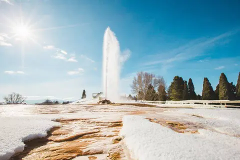 A geyser erupts in a snowy landscape under a bright sunny sky.