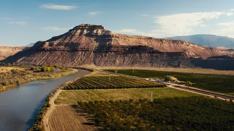 A river flows past agricultural fields beneath a large mesa.