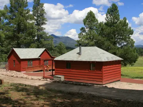 Exterior view of two red cabins set amidst trees and mountains under a cloudy sky.
