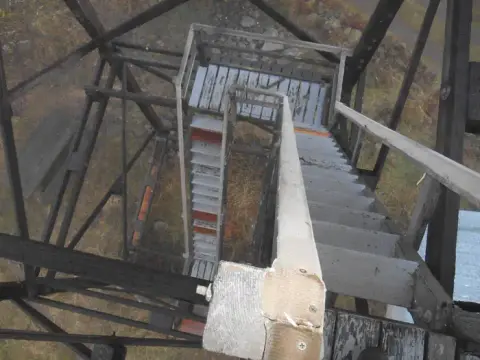 An elevated view looking down a wooden staircase inside an old tower structure.