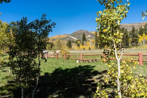 A grassy area with autumn trees and a wooden fence under a blue sky.