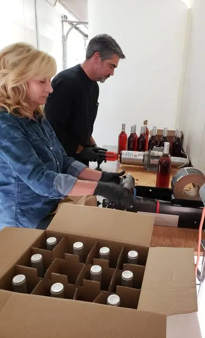 Two people working together to package and label bottles of wine.
