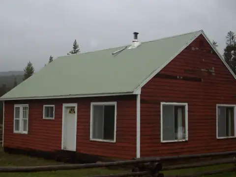 A red wooden cabin with a light green roof stands outdoors.