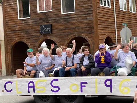 A group of people ride on a parade float in front of a wooden building.