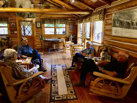 Four people sit and converse in the rustic log interior of a cabin.