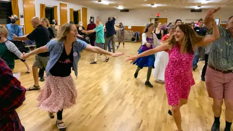 People dancing in an indoor hall with a wooden floor.