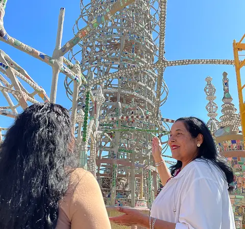 A woman gestures toward an ornate tower structure outdoors.