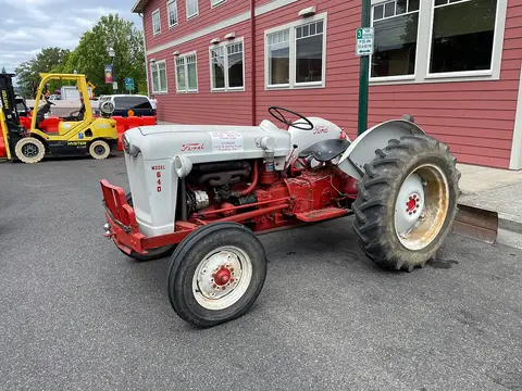 A vintage red and white Ford tractor parked on a paved street.