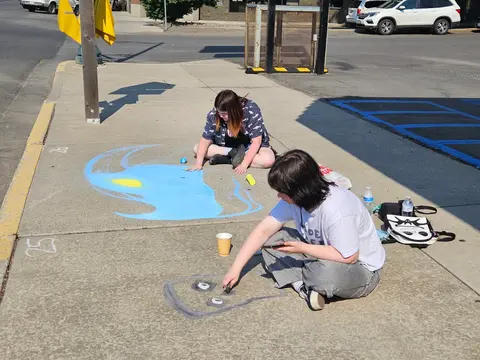 Two people draw with chalk on a concrete sidewalk.