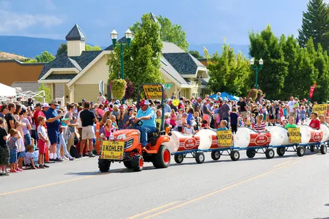 A tractor pulls a train of barrel cars carrying children in a street parade.