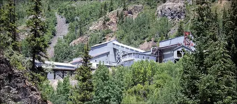 An industrial mining complex nestled among green trees and a rocky mountainside.