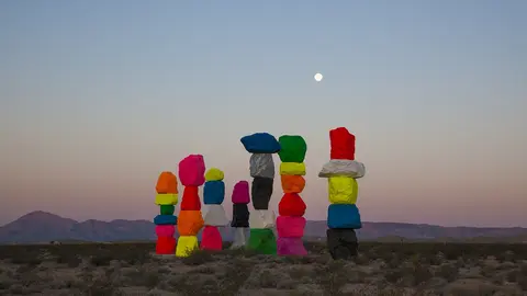 Large brightly colored stacked boulders stand in a desert landscape under the moon.