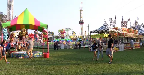 People walk through a carnival with games and food stands.