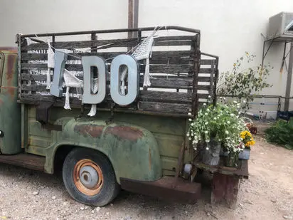 An old green truck decorated with I DO letters on the back.