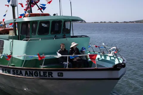 People sitting on the bow of a fishing boat decorated with flags.