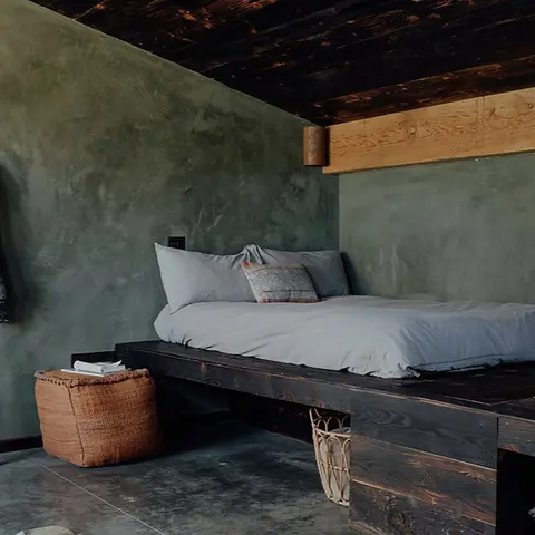 A rustic bedroom with a low wooden platform bed against green walls.