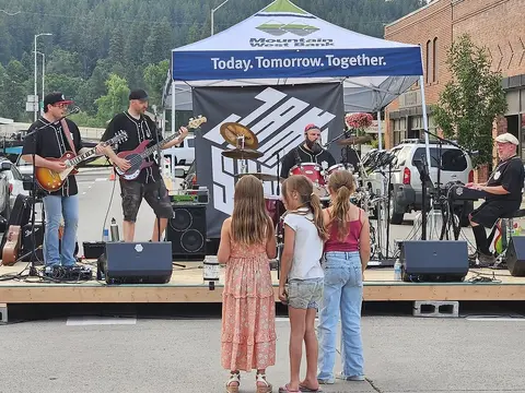A band performs on an outdoor stage with children watching from the front.