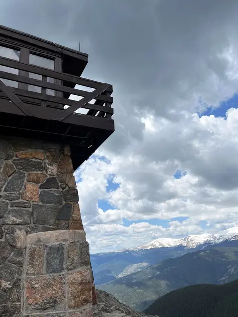 A stone and wood building stands against a cloudy mountain landscape.