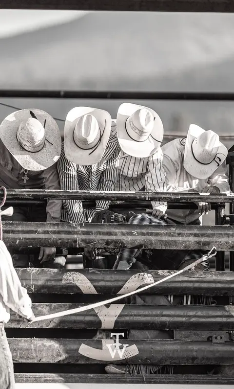 Four people wearing cowboy hats lean over a metal railing outdoors.