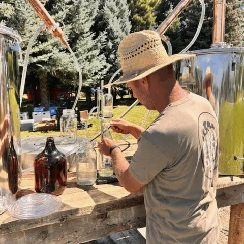 A person operating distilling equipment outdoors.