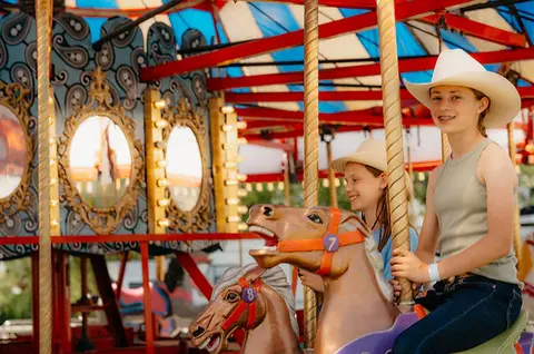 Two girls ride carousel horses at an amusement ride.