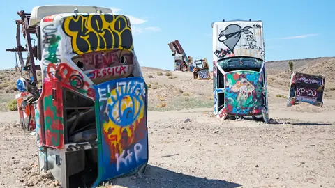 Graffiti-covered vehicles are planted vertically in a desert landscape.