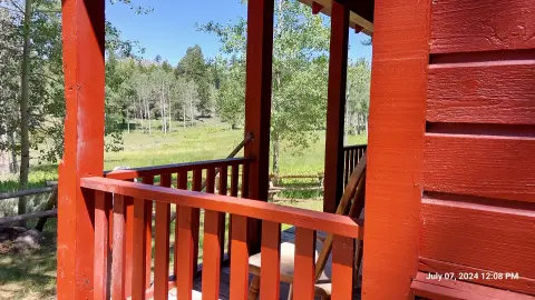 A view of a grassy field and trees from a red cabin porch.
