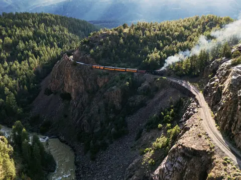 A train travels along a mountain railway line above a canyon and river.