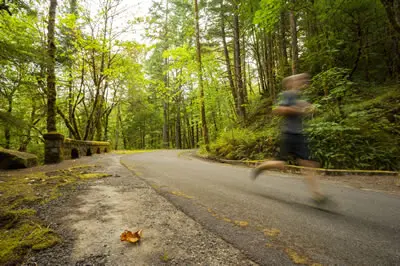 A person running on a paved road through a forest.