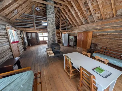 An interior view of a rustic log cabin with a stone fireplace and wooden furniture.