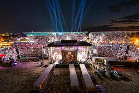 A large crowd fills a stadium at night for a concert with stage lights.