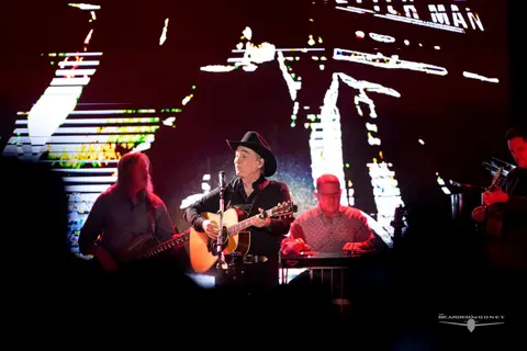 A band performs on a stage with a large digital backdrop.