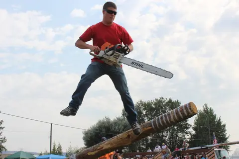 A man balances on a log while holding a chainsaw.