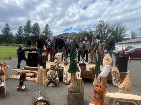 A group of people standing on a stage behind wood carvings outdoors.