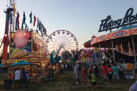A view of a fair with various rides, food stands, and people enjoying the evening.
