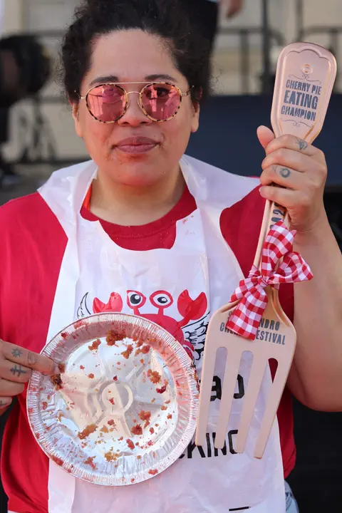 A person holds an empty pie tin and a giant fork after a pie-eating contest.